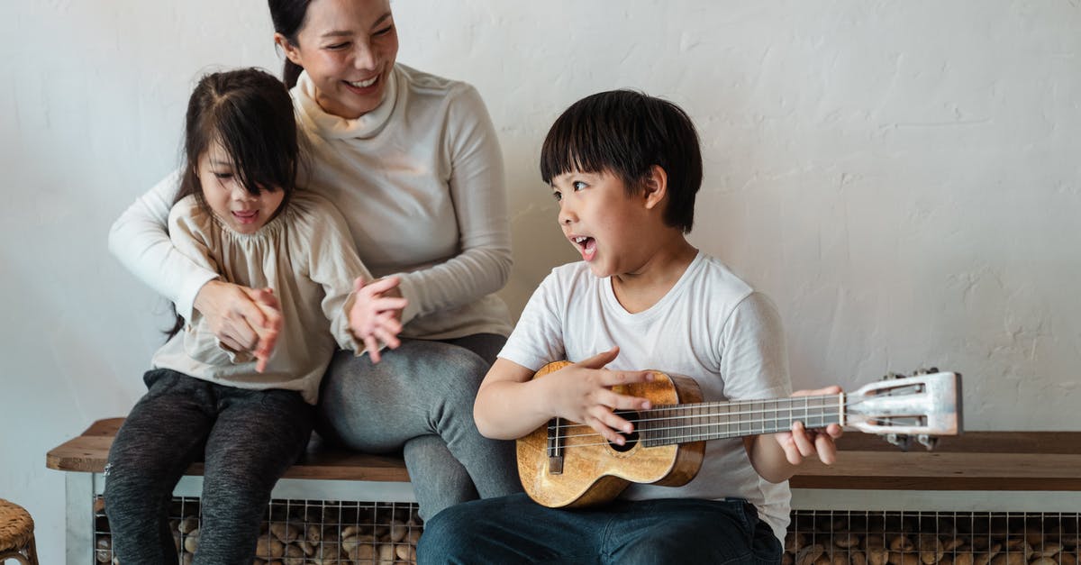 Children of U.K. Passport holder on accompaniment visas - Ethnic boy playing ukulele while sitting with mother and sister