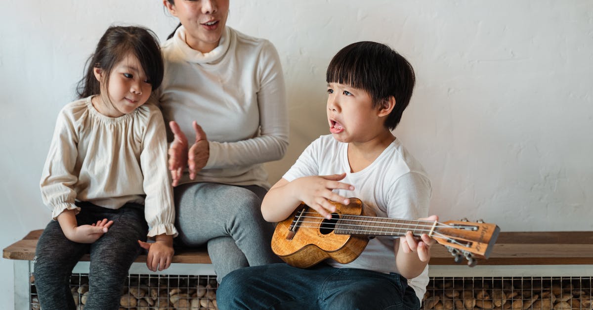 Children of U.K. Passport holder on accompaniment visas - Ethnic boy making grimace while playing ukulele for mother