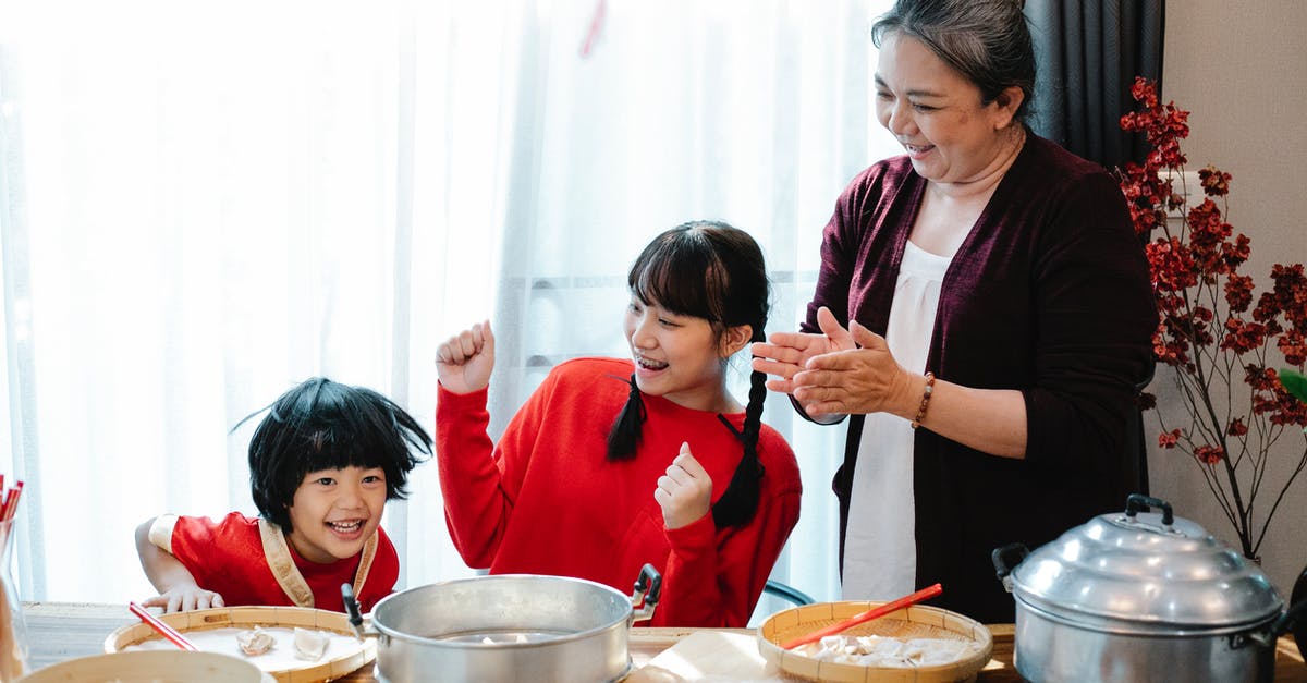 Chinese visiting England, have Schengen visa - Cheerful mature Asian woman with teenage granddaughter clapping hands while having fun with little boy helping with jiaozi preparation in kitchen