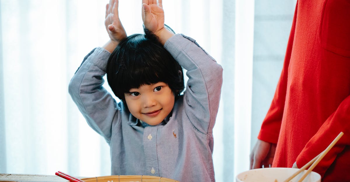 Chinese visiting England, have Schengen visa - Positive Asian kid making bunny ears with hands with hands in kitchen