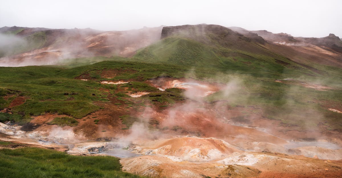 Closest place to Addis Ababa where you can see wildlife - Hilled country with geysers blowing steam off among grass area against volcanic mountains in cloudy day