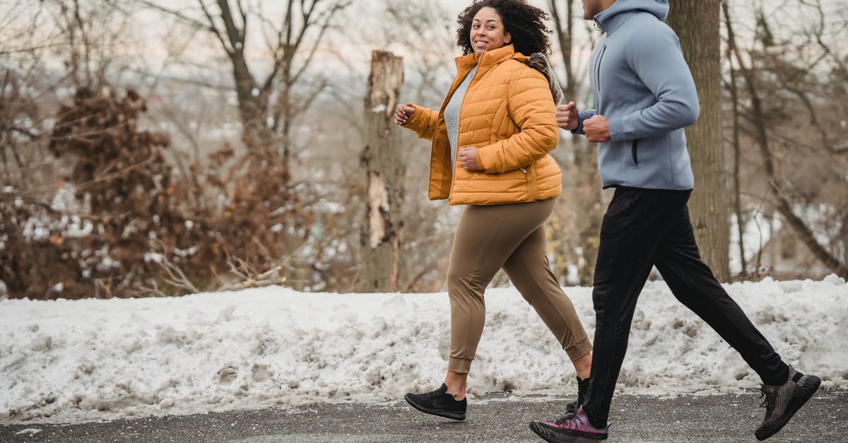 Coach platform positions for trains in Austria - Full body of positive curvy African American woman and black coach looking at each other while jogging on asphalt walkway in winter time
