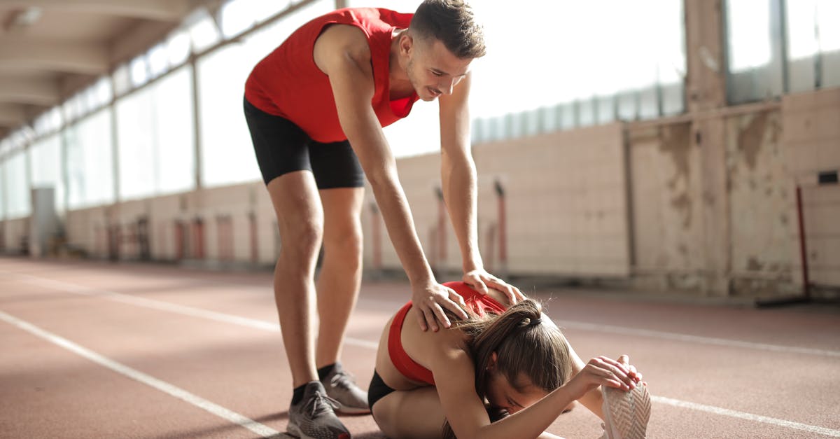 Coach platform positions for trains in Austria - Professional male sportsman helping woman touching knees with head while female sitting on running track and doing stretching exercise