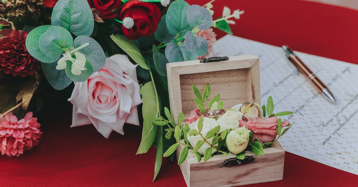 Combination of names on passport differs from marriage certificate - From above of small box with wedding rings near bouquet of flowers and paper on red table