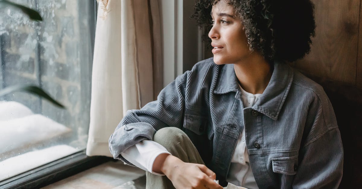 Commuting from Frankfurt to Bad Homburg - High angle of upset African American female suffering from loss and misfortune sitting on windowsill and looking away