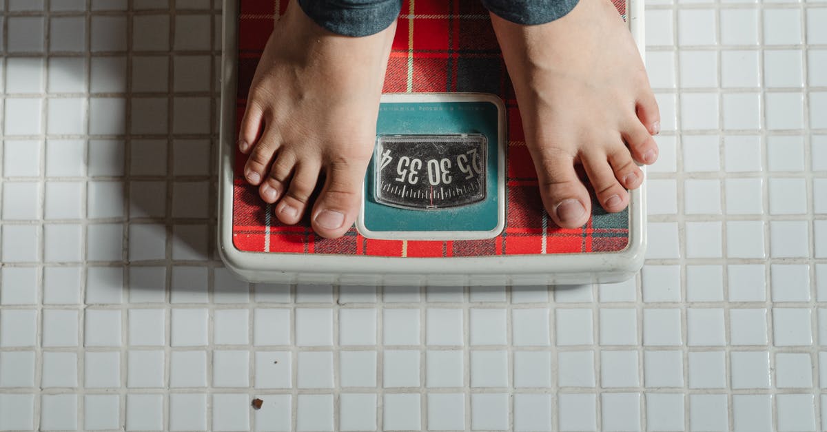 Compact, portable alternative to a bathroom scale - From above crop anonymous barefoot child in jeans standing on weigh scales on tiled floor of bathroom