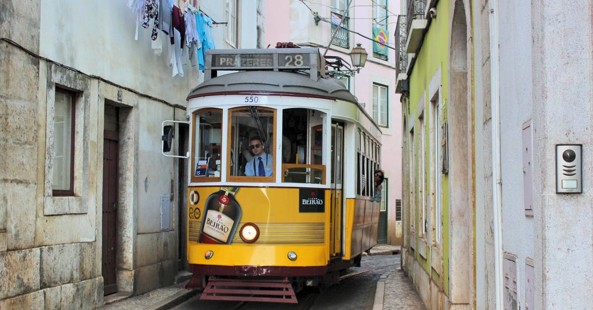 Comparing travel costs in Europe: rail vs bus - Famous old fashioned number 28 Lisbon tram in narrow street of Lisbon with shabby buildings