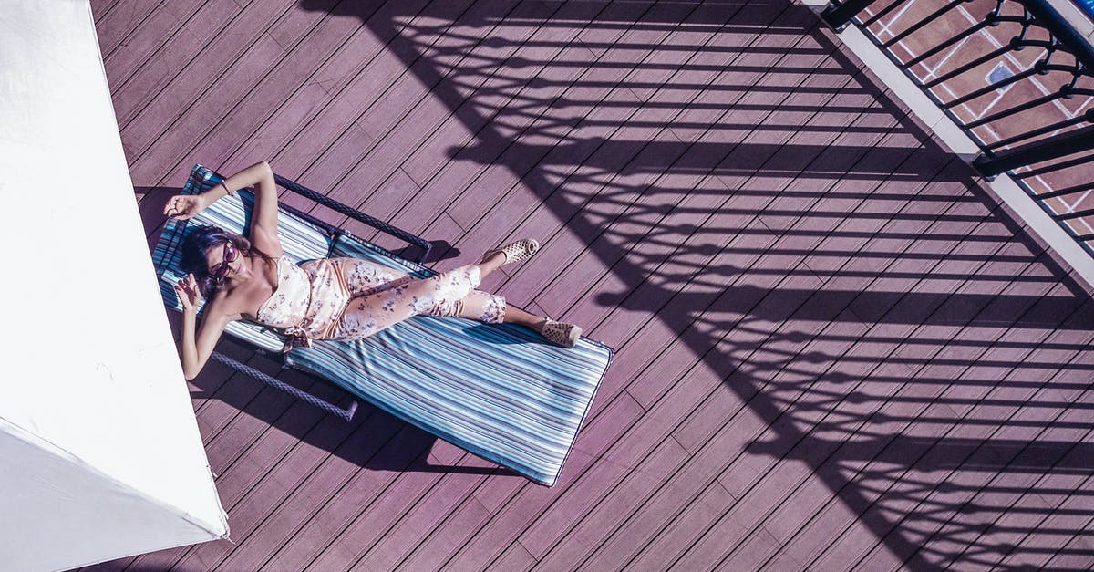 Compensation from hotel - Top view of anonymous female traveler in sunglasses lying with crossed legs on sun bed on wooden floor near fence of hotel balcony in sunlight during trip