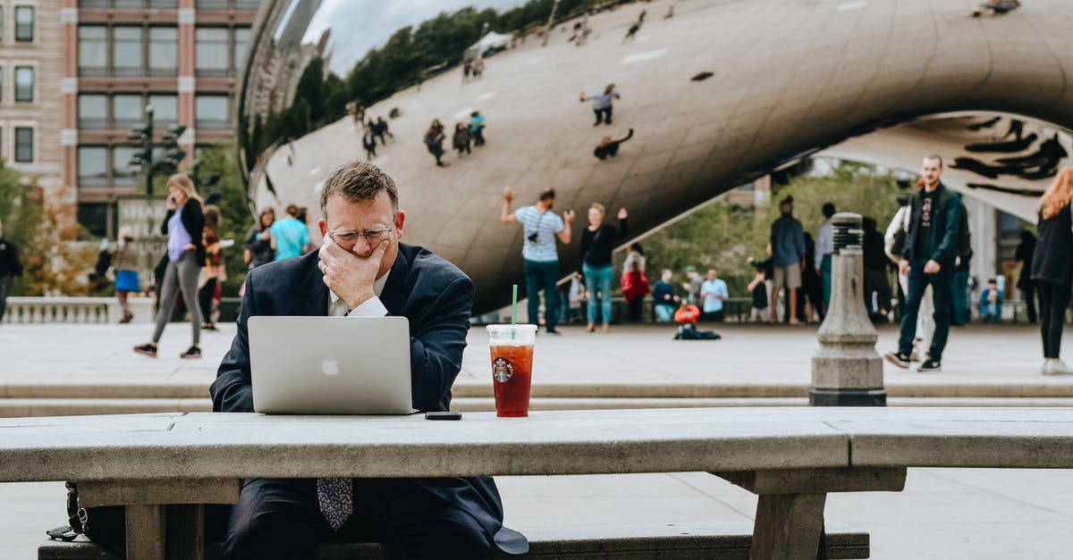 Connecting flight in Chicago - Concentrated businessman in suit touching face and sitting at table with laptop and takeaway drink against modern art sculpture Cloud Gate in Chicago in daytime