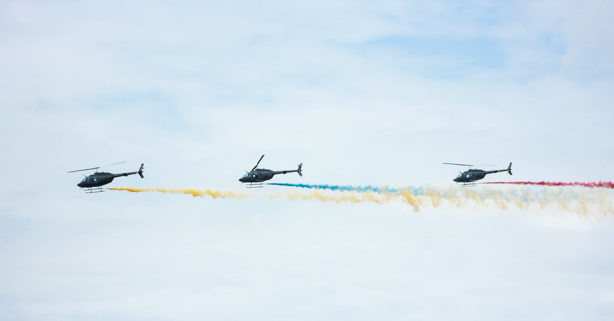 Connecting flight with long layover in Korea - From below of identical black helicopters with long tails and propellers flying in cloudy sky while leaving colorful wavy traces with smoke effect in daylight