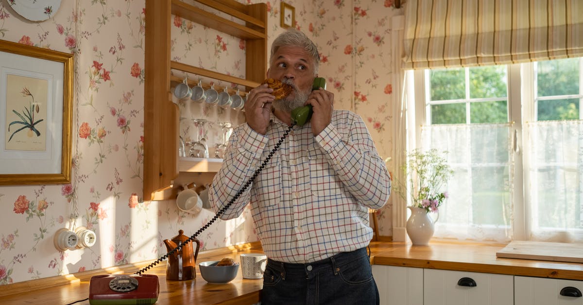 Connecting flights (domestic) on separate tickets with no checked baggage - Senior Man Talking on Landline Phone and Eating Cinnamon Bun in Old-Fashioned Kitchen