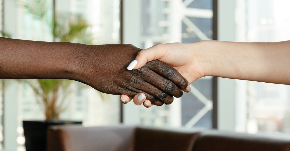 Connecting flights with partner airlines - Crop anonymous diverse women shaking hands together on blurred background of contemporary office