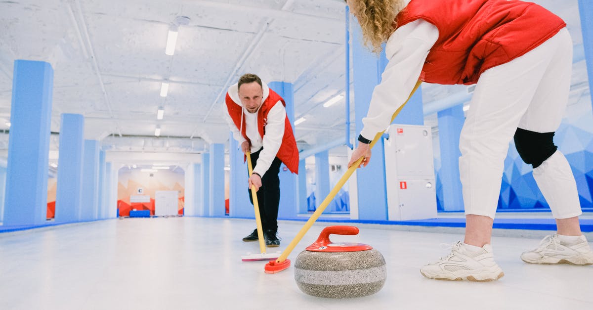 Connecting from ICE to regional trains (Deutsche Bahn) - Low angle of male and female players sweeping ice sheet with brooms in path of granite stone during curling training