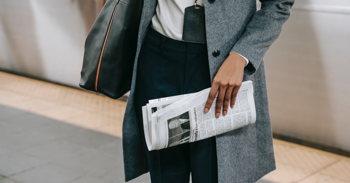 Connecting from Terminal 3 to 1 at Copenhagen CPH - From above of crop anonymous female employee in elegant outfit and name tag standing on platform of metro station with newspaper in hand