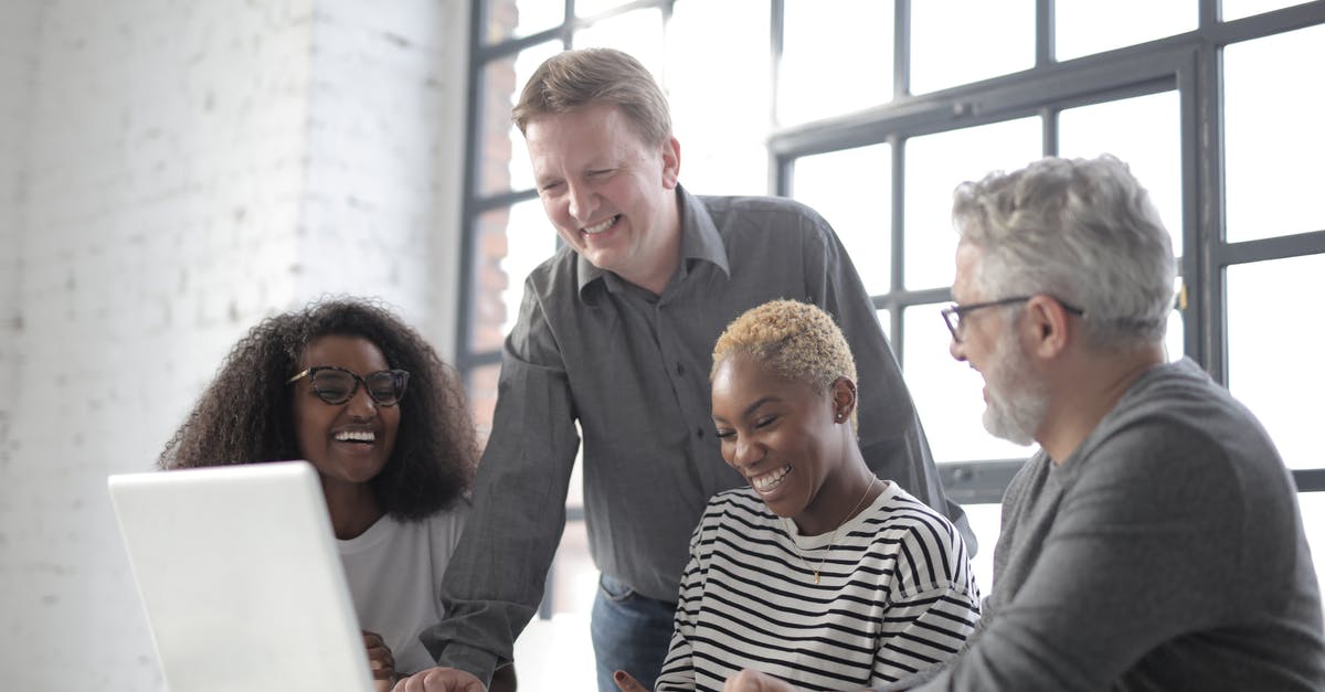 Connecting in Amsterdam with different airlines - Group of diverse people laughing and using netbook while working on project together in office with white brick walls and big window