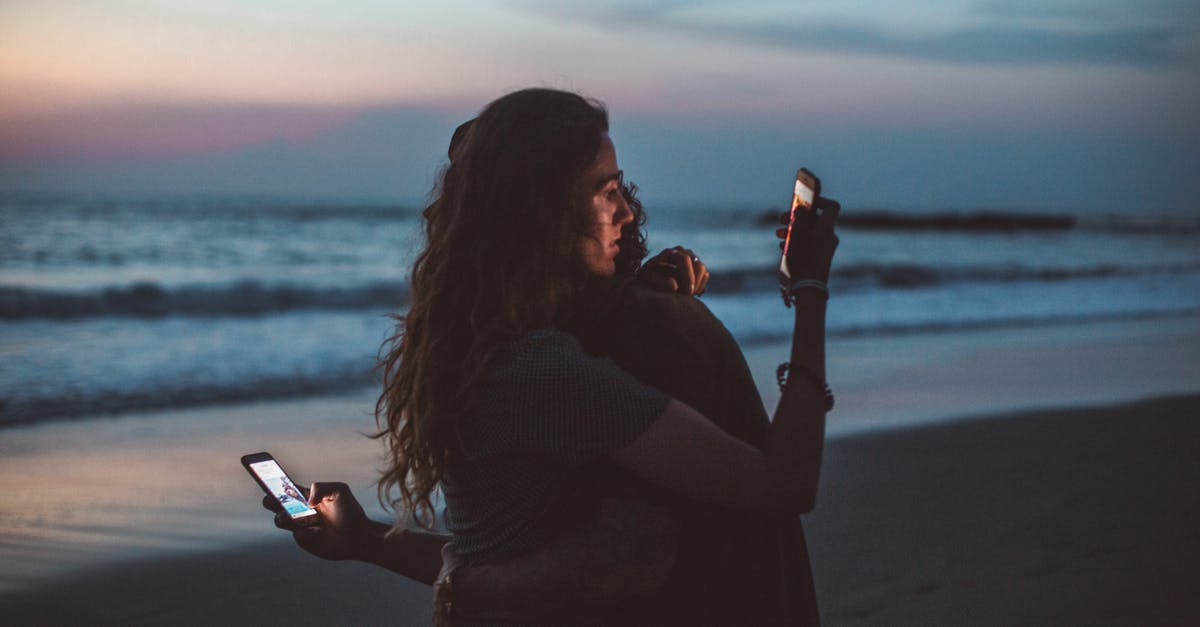 Connecting in Liverpool on separate tickets with carry-on only - Couple hugging and using smartphone near sea on sunset