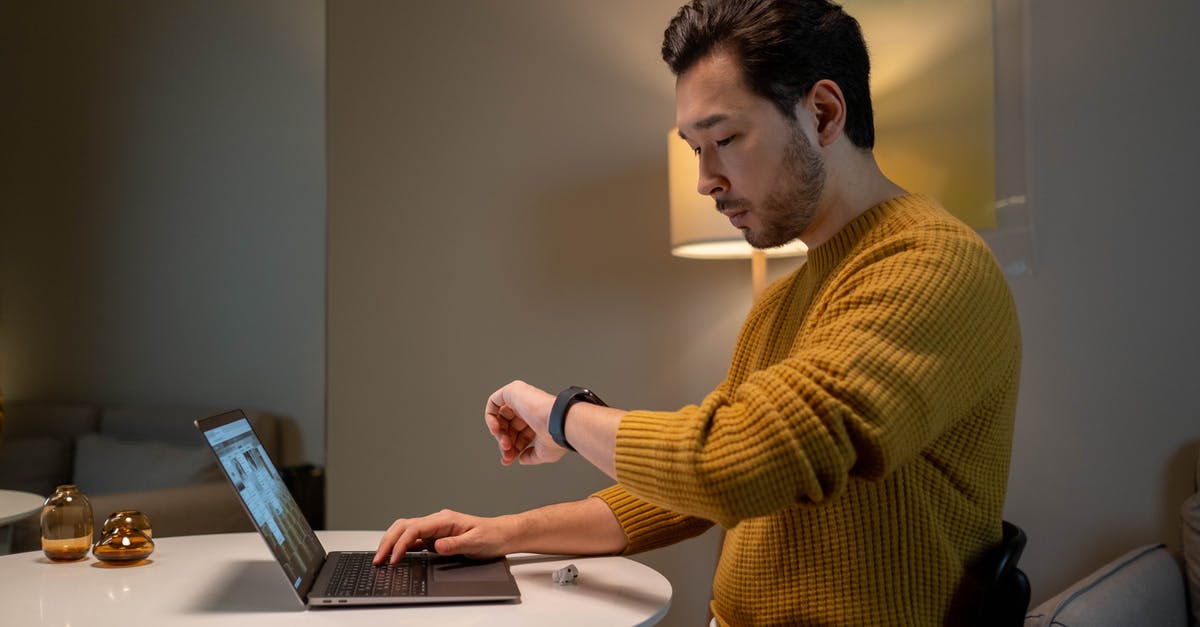 Connecting time ay JFK - Man in Brown Sweater Looking at Time on His Smartwatch while Using Laptop