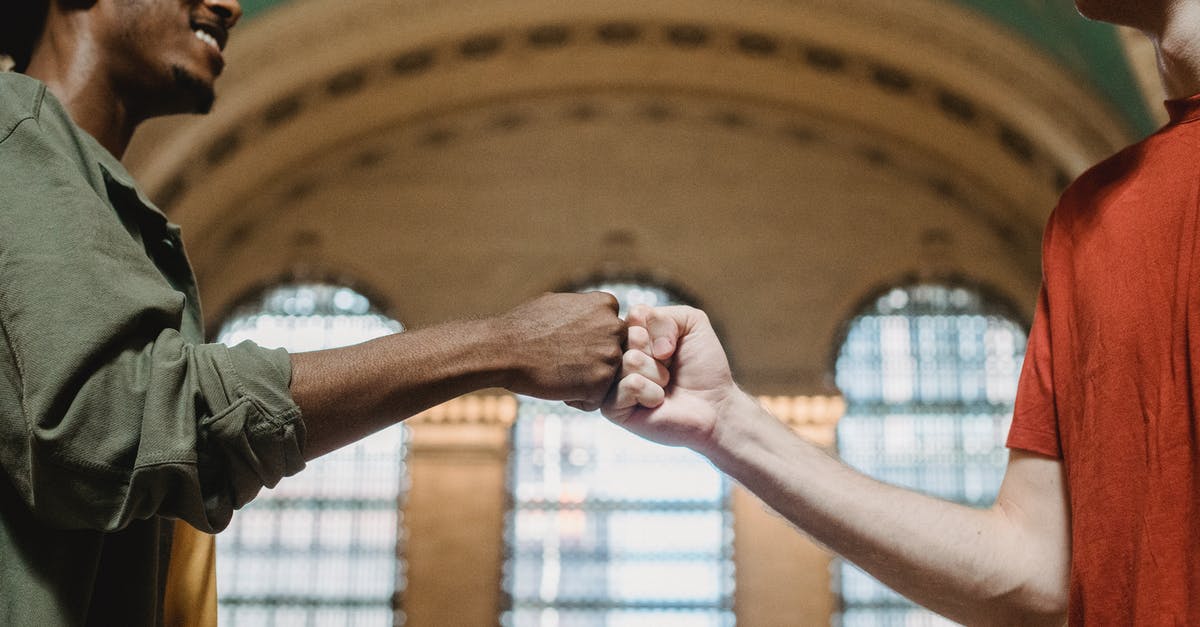 Connection time needed from USA to Heathrow to Shannon - From below of crop multiethnic friends in casual clothes giving fist bump against arched wall and windows in aged hallway of Grand Central Terminal placed in New York City