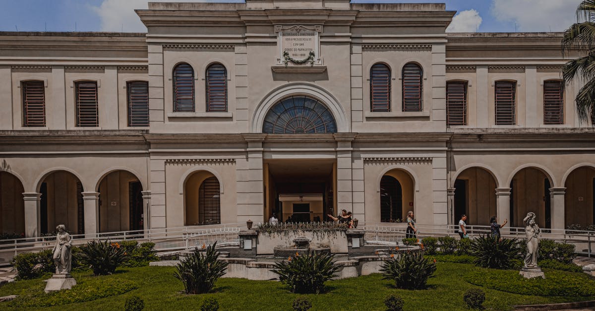 Consequences of immigration delays - Old museum facade against sculptures on lawn in city