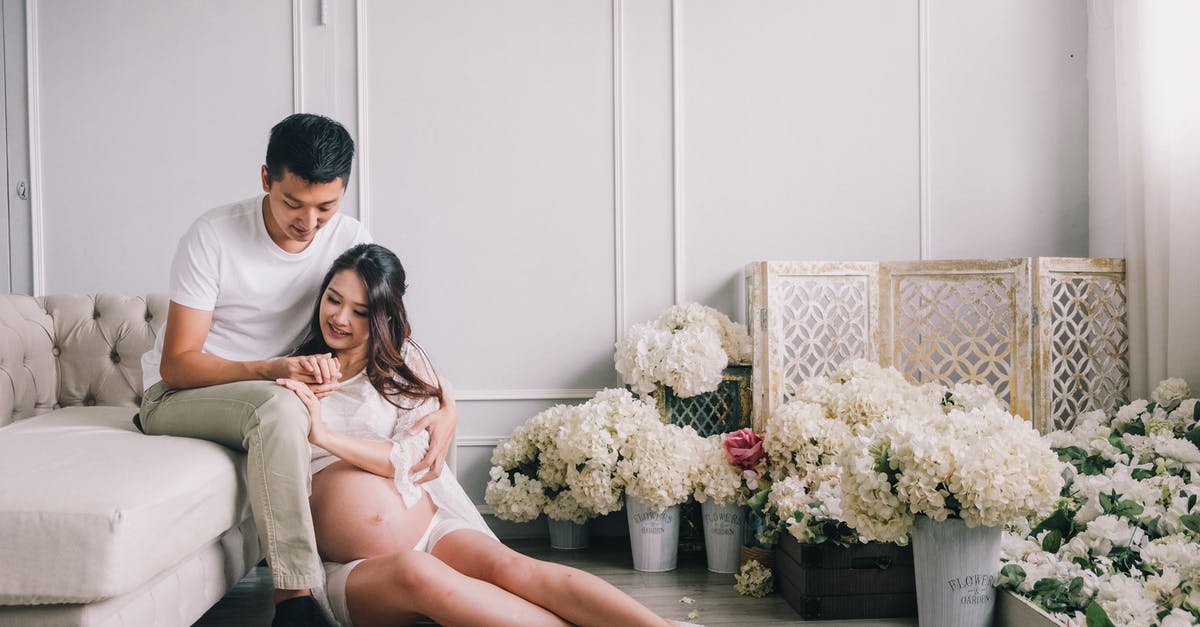 Country to live in for ~2 months when pregnant [closed] - Happy young Asian male and pregnant female sitting together among white flowers in elegant living room