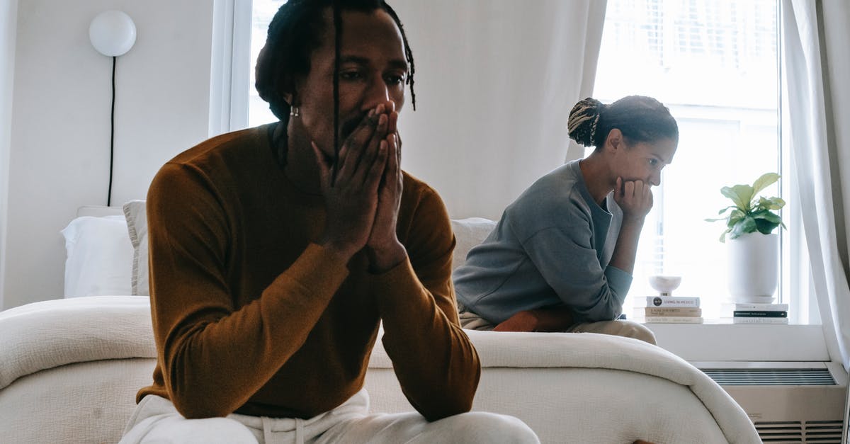 Couple applying for UK tourist visa in separate countries - Wistful concerned African American couple in casual clothing sitting on bed at home after having quarrel