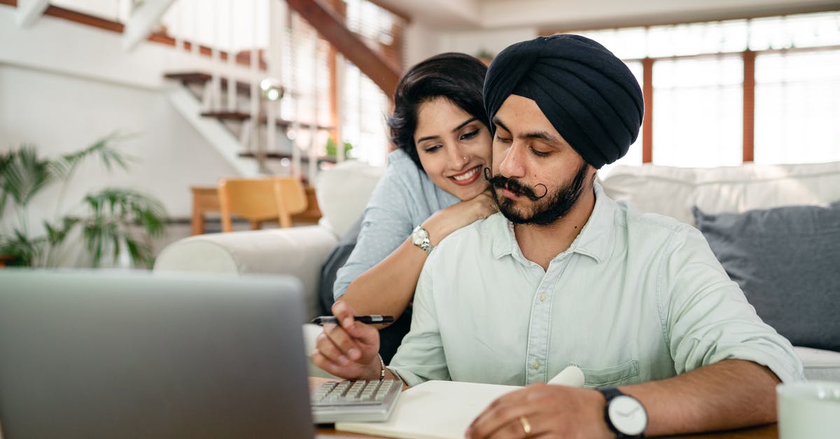 Cover letter for spouse travelling with husband on business visa - Cheerful young Indian woman cuddling and supporting serious husband working at home with laptop and counting on calculator