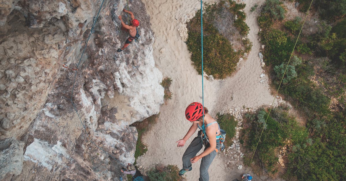 Coverage of unusual activities with travel insurance - From above of anonymous people hanging on ropes while climbing on stony cliffs with green bushes