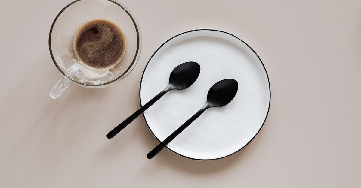 Crossing border from India to Myanmar - From above composition of ceramic plate with black spoons placed near glass cup of coffee on beige table