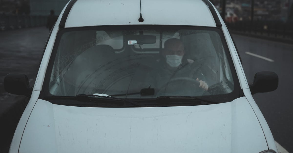 Crossing from UK to France and back on the same day in the same car but with different drivers - From above of unrecognizable male in medical mask driving white car on street on gloomy cloudy day during coronavirus Crossing from UK to France and back on the same day in the same car but with different drivers - From above of unrecognizable male in medical mask driving white car on street on gloomy cloudy day during coronavirus
