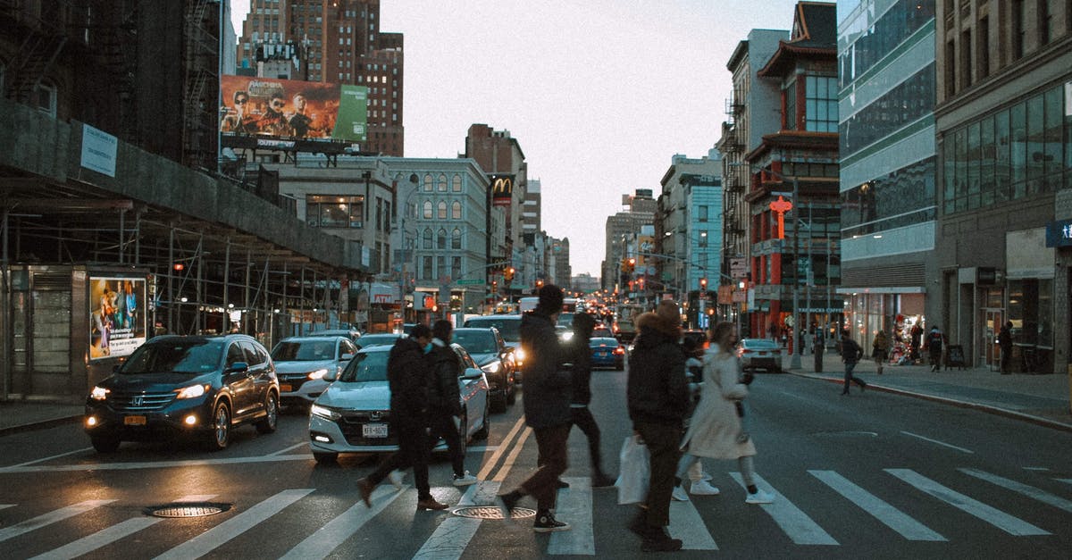 Crossing the Amazon, route 319 - Group of people walking on pedestrian crossing on asphalt road with cars in city with residential buildings in evening time