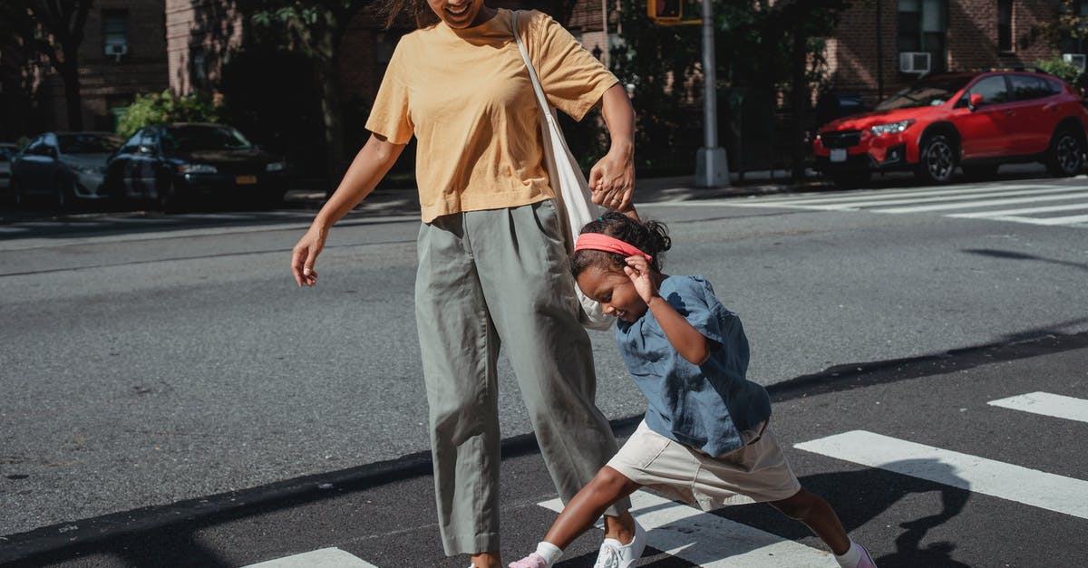 Crossing the road in London - Did I have 'right of way'? - Full body of ethnic woman and little girl holding hands and having fun while walking on pedestrian crossing on sunny street