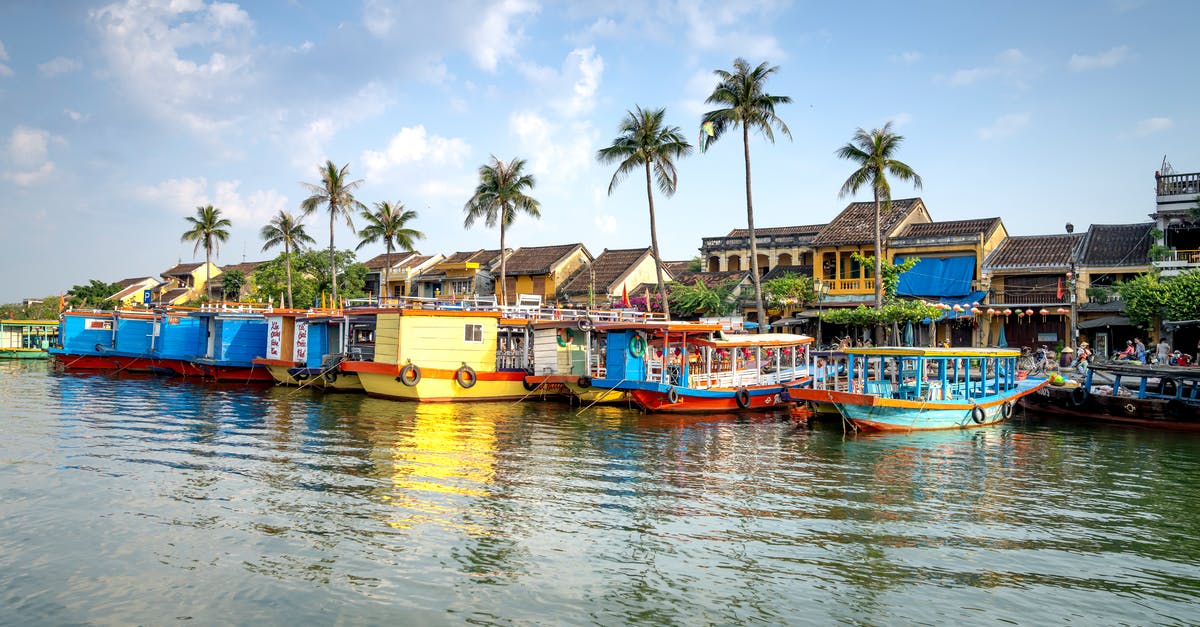 Cruising to Vietnam - Typical colorful boats moored on Thu Bon River near residential houses against blue sky in Hoi An