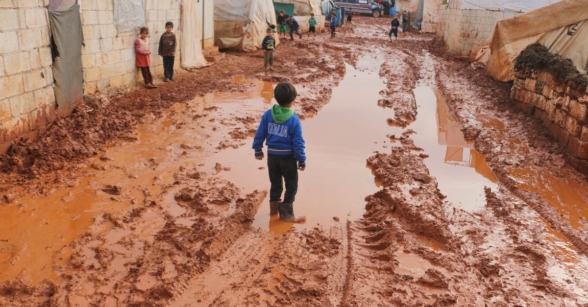 Cumbria Way in June. Do I need to make reservations? - Group of children standing on dirty wet ground with puddles between old tents in refugee camp with in poor settlement