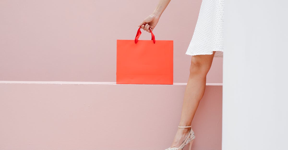 Customs and immigration clearance transiting at DEL - Crop anonymous stylish female in white dress and high heels carrying red shopping bag against pink wall