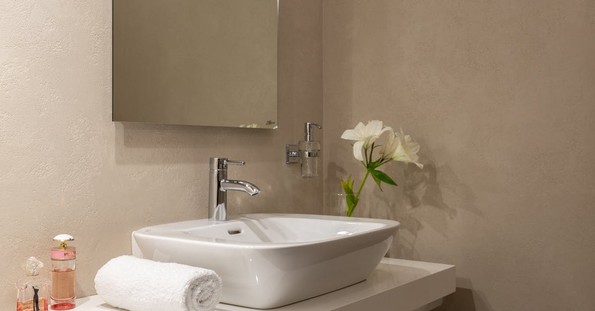 Daily tipping hotel staff in coins (US) - Interior of bathroom with white wrapped towel near ceramic basin and faucet with mirror on wall