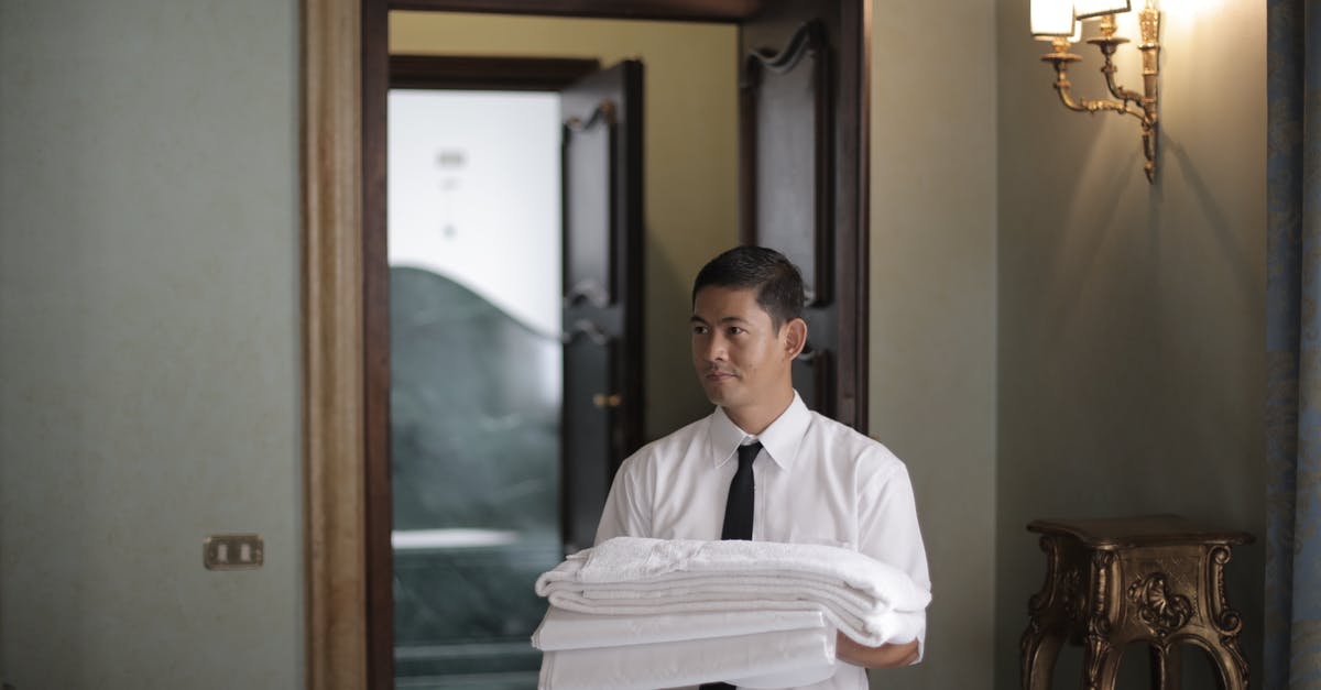 Daily tipping hotel staff in coins (US) - Young male housekeeper carrying stack of white bed sheets while entering bedroom in hotel