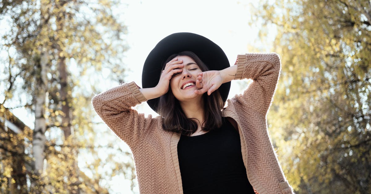 Day Tours from Within Kazbegi / Stepantsminda [closed] - Low angle of smiling female with closed eyes in knitted cardigan and black hat touching face while standing on sunny autumn day