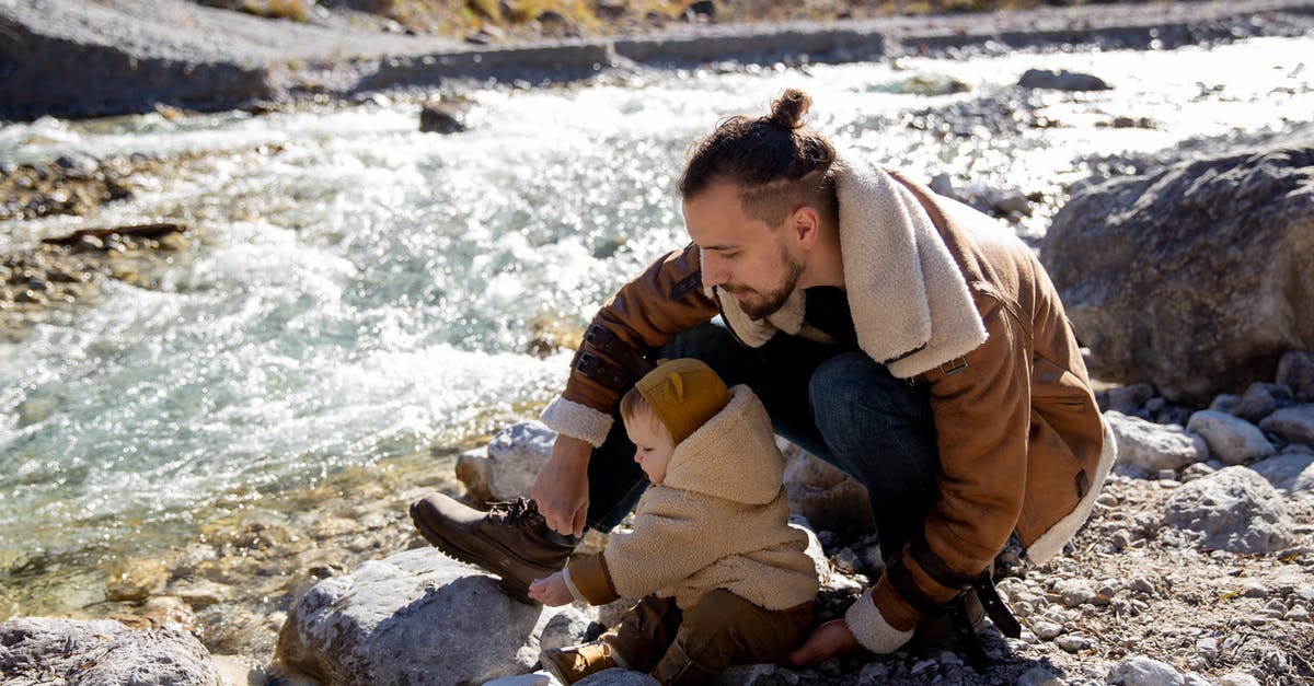 Day trip or weekend trip from Vientiane, Laos? - Bearded young father with little child in casual warm clothes sitting on rocky ground near river and enjoying time together while weekend