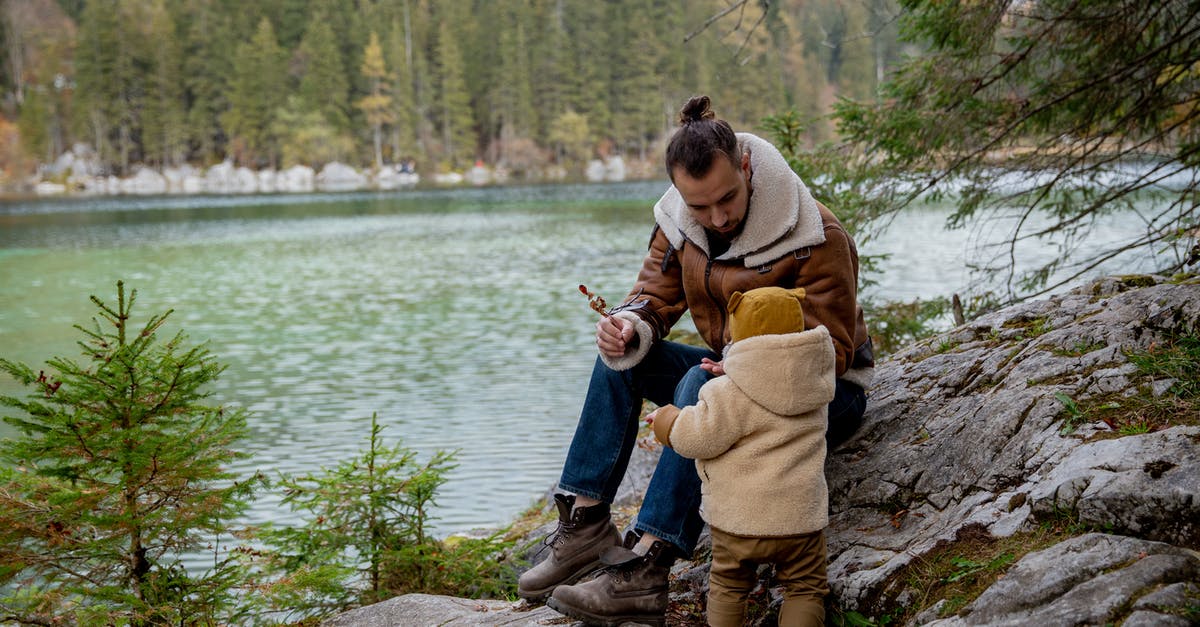 Day trip or weekend trip from Vientiane, Laos? - Father and little kid in casual warm clothes resting on rocky ground near lake in calm forest on overcast day in autumn