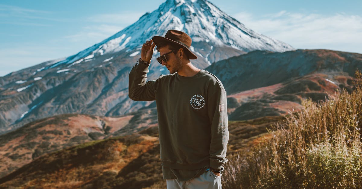 Day trip to castle(s) when staying in Bucharest - Young stylish man in hat and modern sunglasses standing on hill with hand in pocket against high snowy mountain