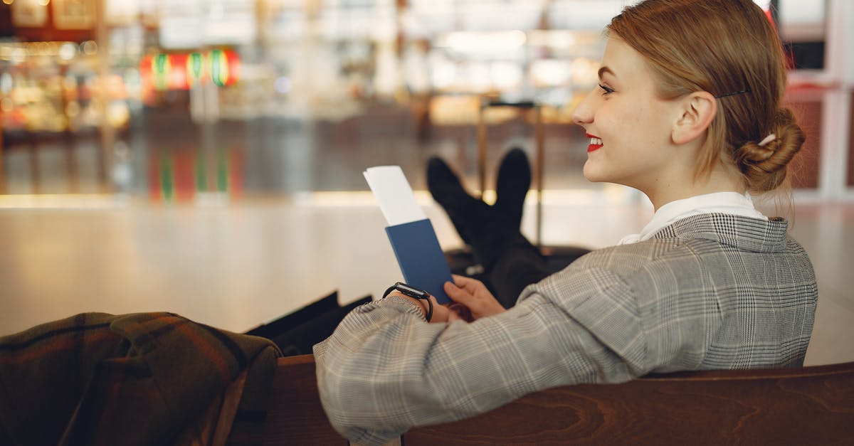 Delay compensation for multi-legged flight - Side view of cheerful female student in checkered jacket smiling away while chilling in hall with outstretched legs and passport in hands