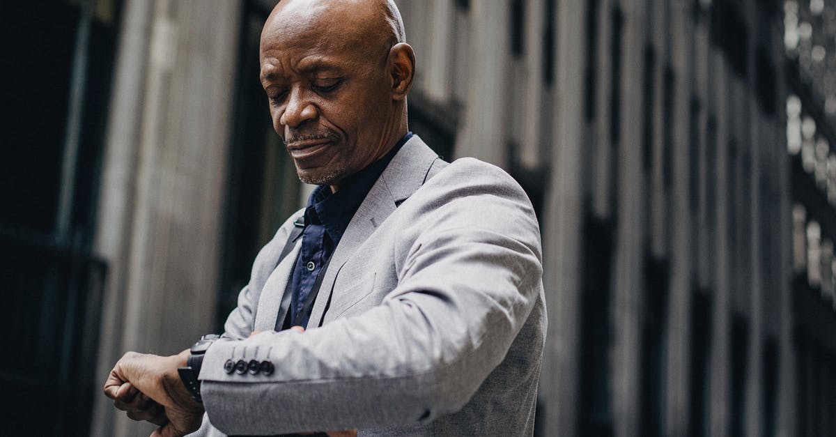 Delays in SFO in late February - Serious African American businessman in formal suit looking at wristwatch while standing outside modern business center building