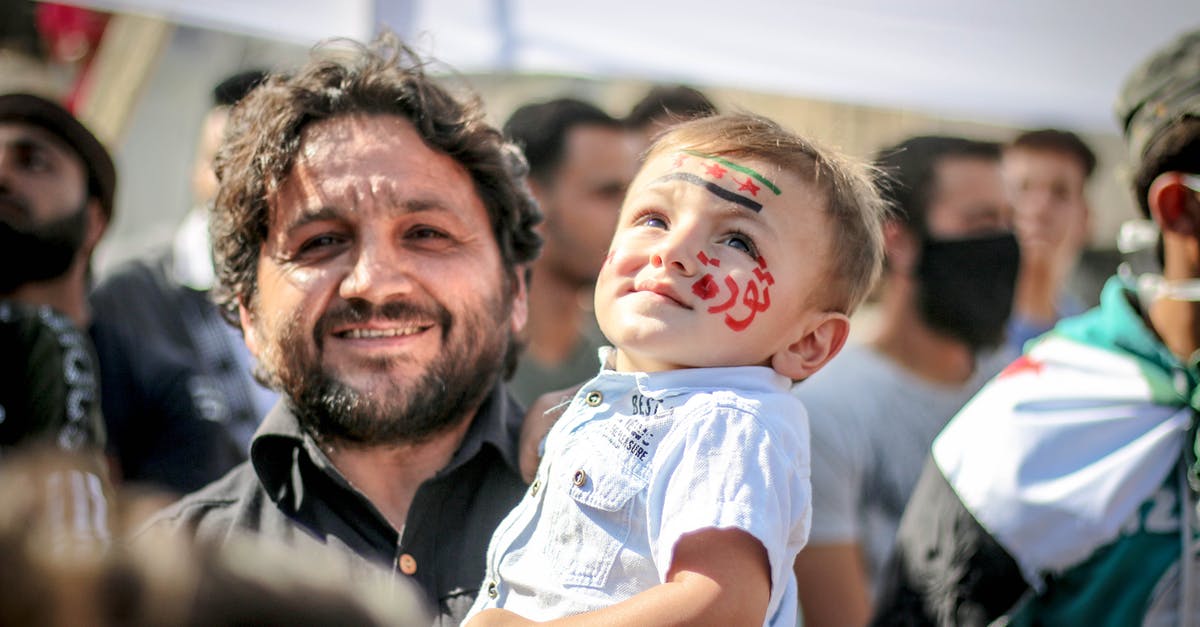 Delta carry-on policy - Ethnic bearded man carrying small kid with painted face in crowd of protesting against policy