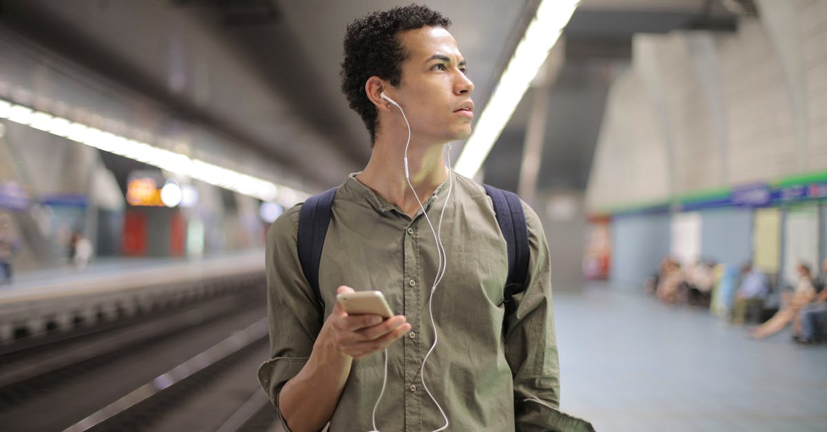 Denver airport public transport - Young ethnic man in earbuds listening to music while waiting for transport at contemporary subway station