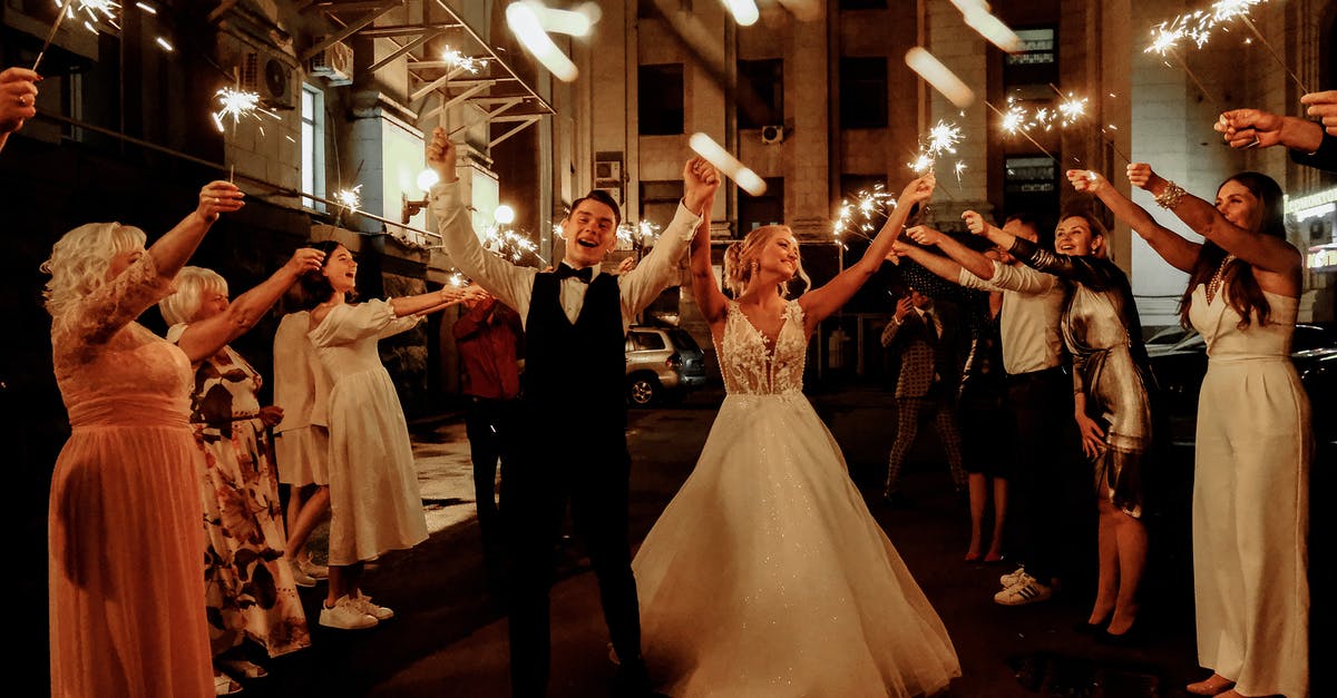 Dependent wife with no marriage certificate: UK visa - Cheerful young bride and groom with guests dancing on street with sparklers in hands during wedding party