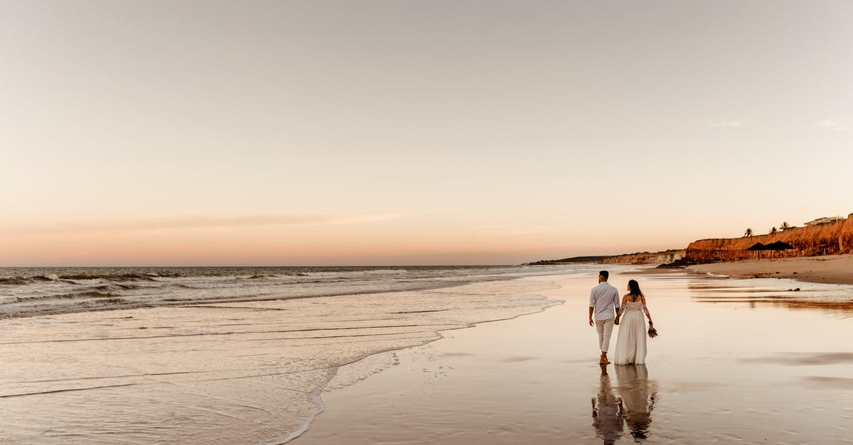 Dependent wife with no marriage certificate: UK visa - Back view of barefoot groom holding hand of bride in white dress and walking together on sandy coast