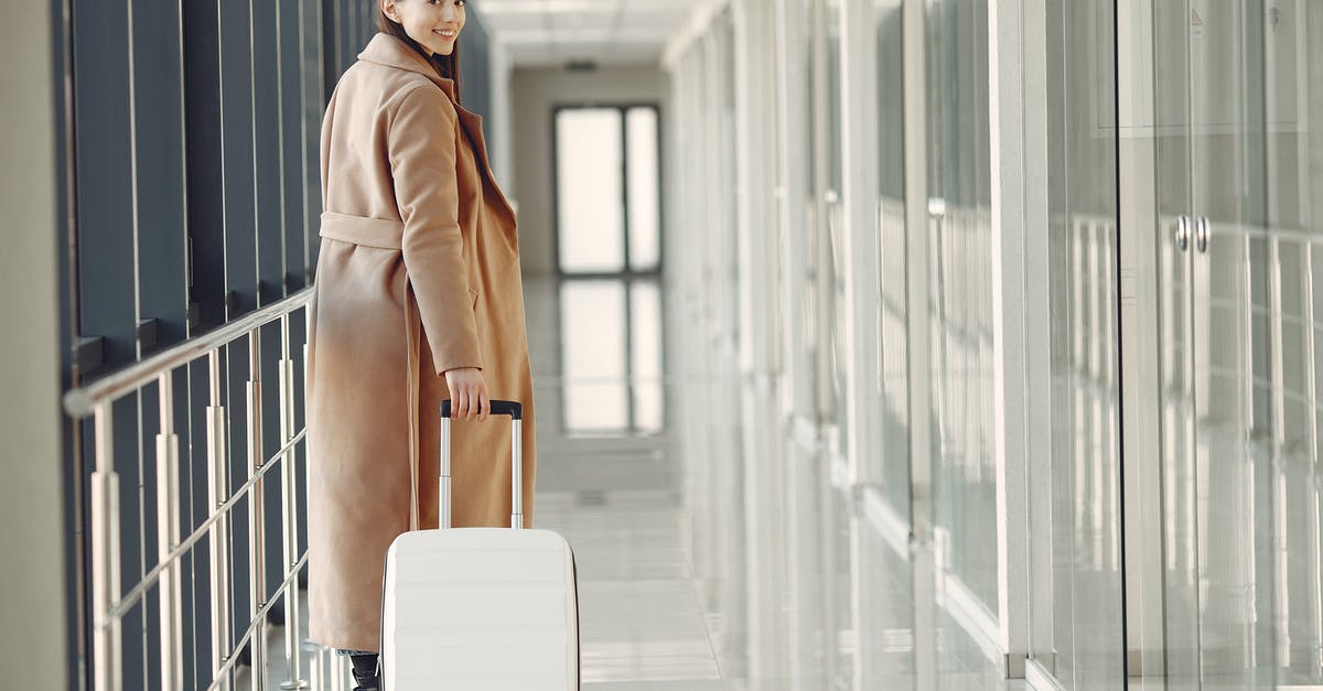 Determine gate for departing Heathrow flight - Stylish happy traveler with suitcase in airport hallway