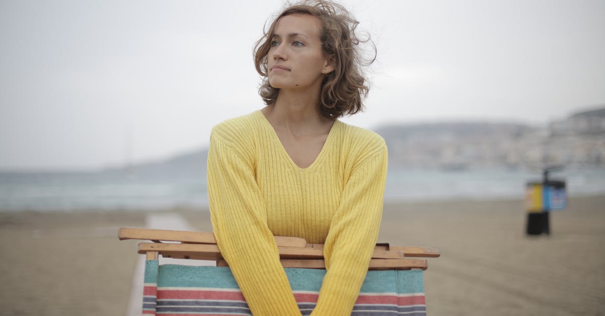 Did I miss something? - Calm female tourist with folded deckchair standing alone on seashore in overcast weather