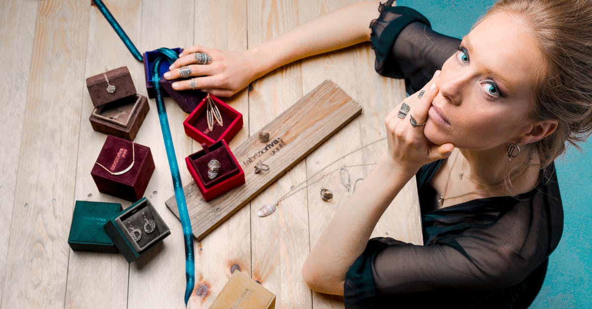 Did not declare jewelry from Aruba - From above serious businesswoman looking up at camera while sitting at wooden table with small jewelry boxes with bijouterie and decorating with ribbon as present