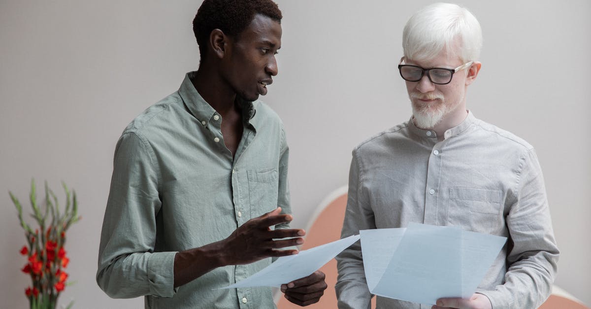 Different controls on document on the same route - Concentrated African American man and albino coworker in eyeglasses working with papers while discussing work in contemporary office with flower